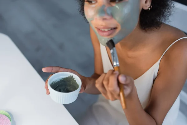 Vista ritagliata della donna afro-americana che applica maschera di argilla a casa — Foto stock
