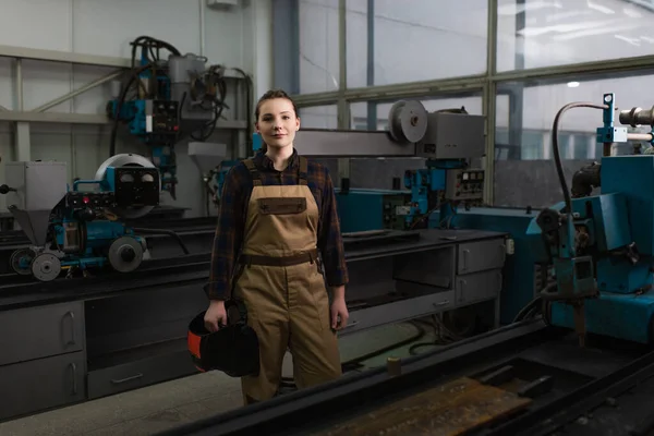 Welder holding welding mask near machinery in factory — Foto stock