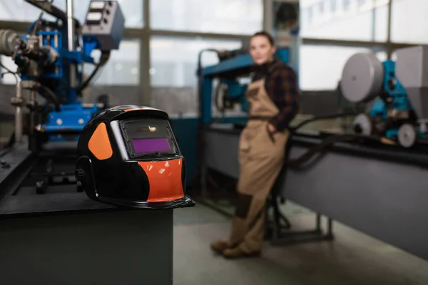 Welding mask on machine near blurred welder in factory — Stock Photo