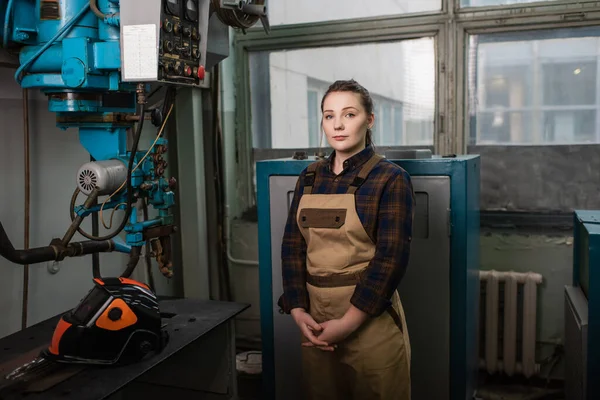 Soudeur en salopette debout près de la machine à souder et masque de protection en usine — Photo de stock