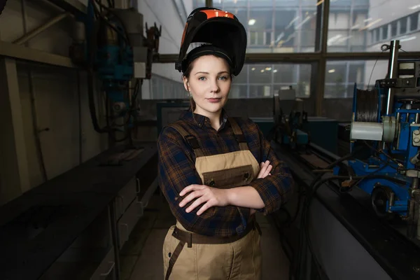 Young welder in protective mask looking at camera while crossing arms in factory — Stock Photo