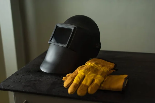Máscara de soldadura con visera y guantes en la mesa en fábrica - foto de stock