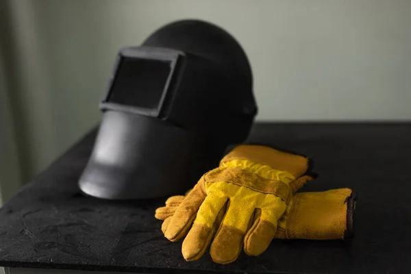 Guantes de soldadura cerca de máscara borrosa en la mesa en fábrica - foto de stock