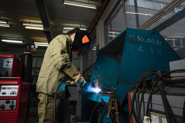 Soudeur en uniforme et gants travaillant avec torche de soudage près de la machine en usine — Photo de stock