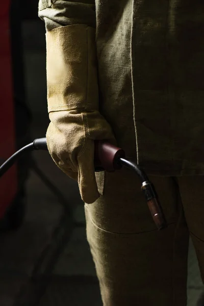 Обрезанный вид сварщика в перчатках и однородной держатель сварочной горелки на заводе — стоковое фото