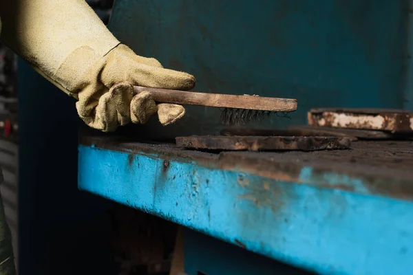 Cropped view of welder in protective glove holding brush above detail in factory — Stock Photo