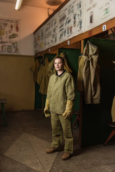 Schweißer in Uniform und Handschuhen blickt in der Garderobe der Fabrik in die Kamera — Stockfoto