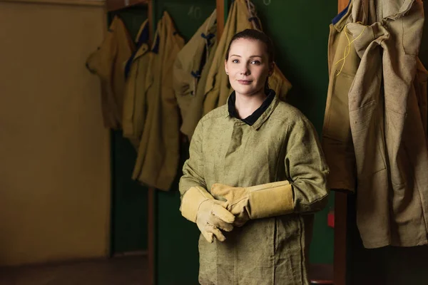 Welder in gloves and uniform looking at camera in dressing room of factory — Stock Photo