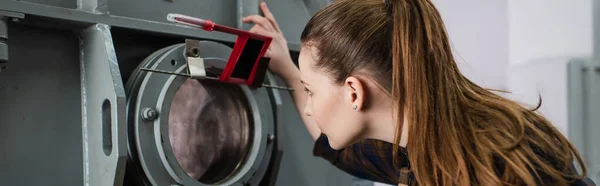 Side view of brunette welder looking at vacuum laser welding machine in factory, banner — Stock Photo