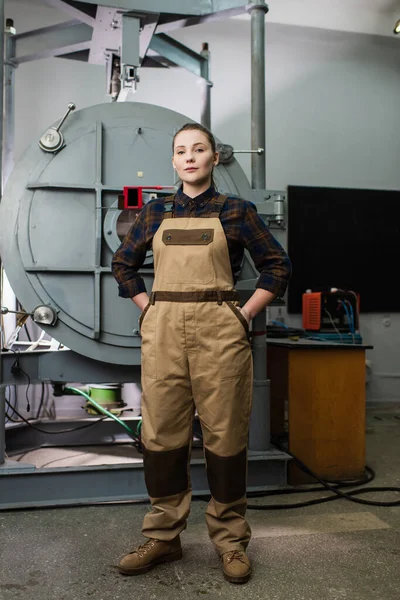 Young welder in overalls looking at camera near vacuum laser welding machine in factory — Foto stock
