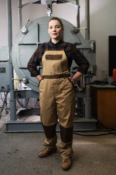 Volle Länge des Schweißers hält Hände in Taschen von Overalls in der Nähe von Vakuum-Laserschweißmaschine in der Fabrik — Stockfoto