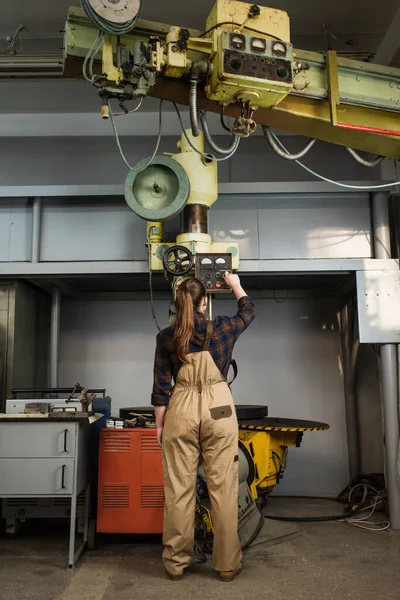 Vue arrière du soudeur en salopette et chemise travaillant sur une machine à souder en usine — Photo de stock