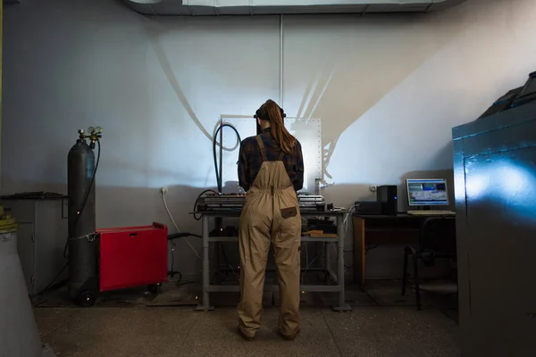 Vue arrière du soudeur brune travaillant à proximité d'une bouteille de gaz et d'un ordinateur en usine — Photo de stock