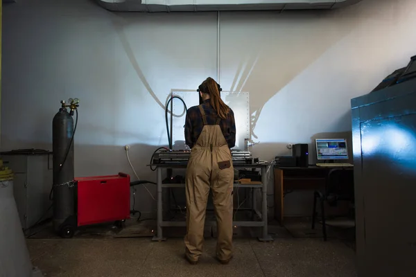 Back view of brunette welder working near gas cylinder and computer in factory — Stock Photo