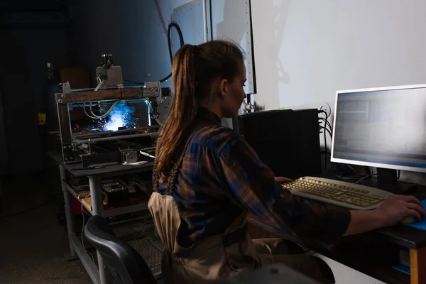 Side view of brunette welder using computer while working near welding machine in factory — Stockfoto