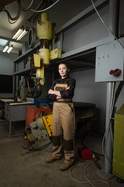 Welder in shirt and overalls looking at camera near welding machine in factory — Foto stock