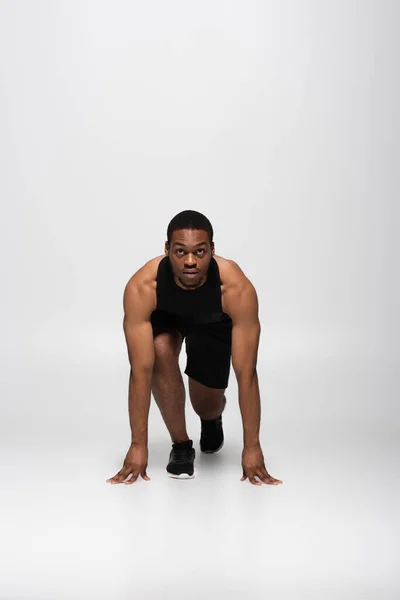 Longueur totale du sportif afro-américain dans la pose de départ avant de courir sur gris — Photo de stock