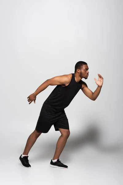 Full length of young african american sportsman running fast on grey — Stockfoto