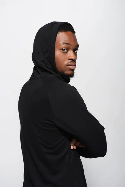 Молодий афроамериканський чоловік в светрі дивиться на камеру, позує схрещеними руками ізольовано на сірому — стокове фото