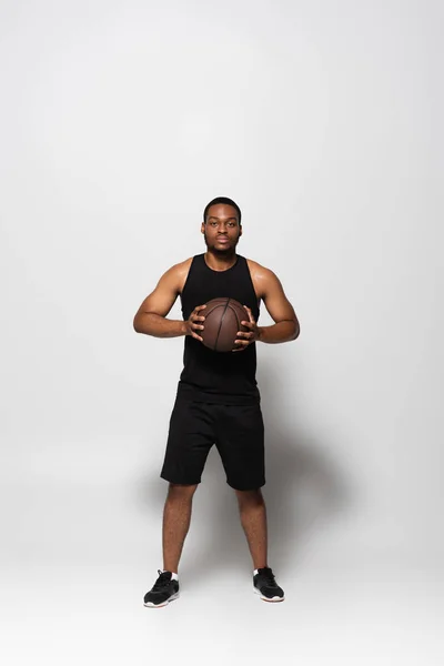 Full length of african american player holding basketball on grey — Stockfoto