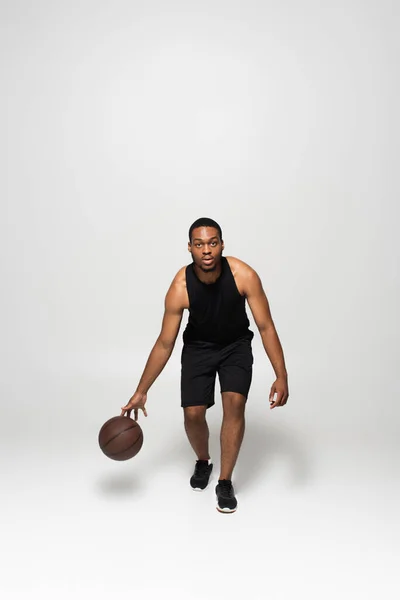 Comprimento total de homem americano africano muscular jogando basquete em cinza — Fotografia de Stock