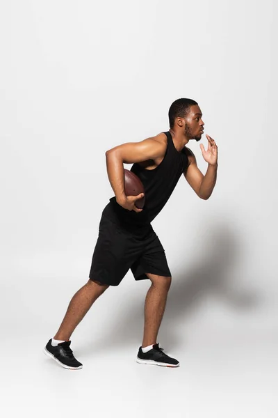 Full length of african american sportsman playing rugby and running on grey — Stock Photo