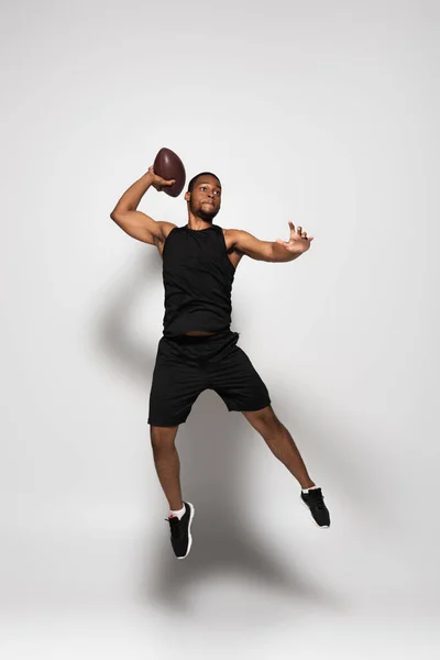 Comprimento total do atleta afro-americano jogando rugby e pulando em cinza — Fotografia de Stock