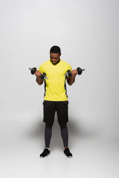 Full length of african american sportsman working out with dumbbells on grey — Stock Photo