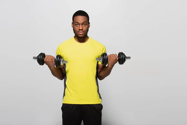 Joven deportista afroamericano haciendo ejercicio con mancuernas aisladas en gris - foto de stock