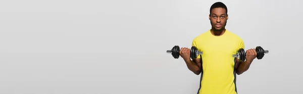 Young african american sportsman working out with dumbbells isolated on grey, banner — Foto stock