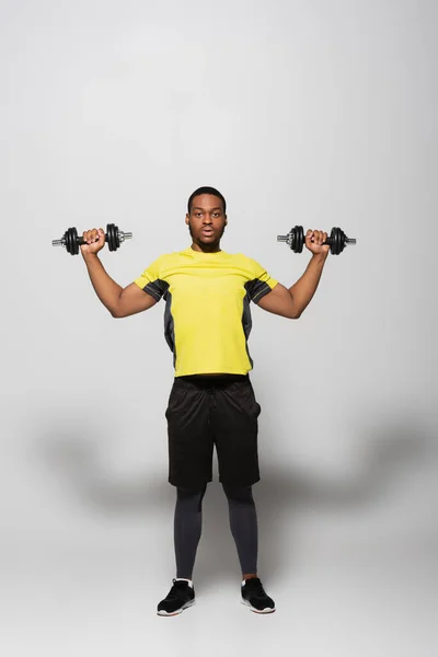 Longitud completa de deportista afroamericano haciendo ejercicio con pesadas mancuernas en gris - foto de stock