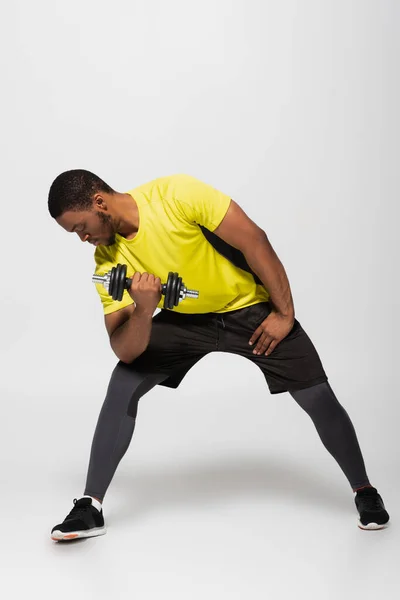 Full length of african american sportsman working out with dumbbell on grey — Stock Photo