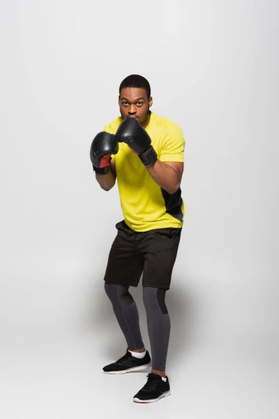Full length of strong african american sportsman in boxing gloves on grey — Stock Photo