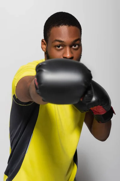 Strong african american sportsman exercising in boxing gloves isolated on grey — Stockfoto