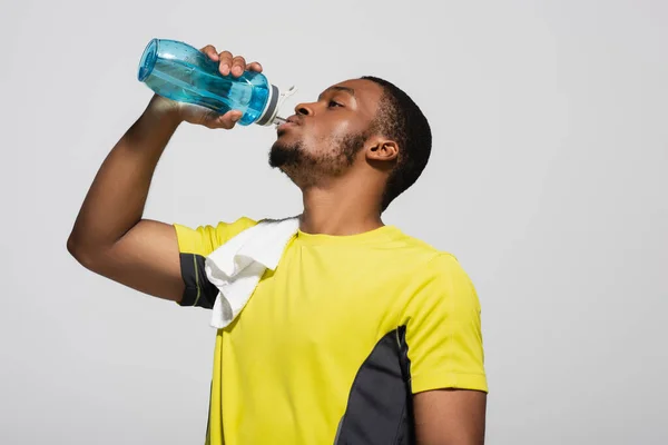 African american sportsman drinking water from sports bottle isolated on grey — Stock Photo