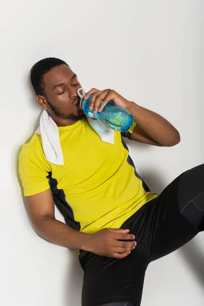 High angle view of african american sportsman drinking water from sports bottle on grey — Stockfoto