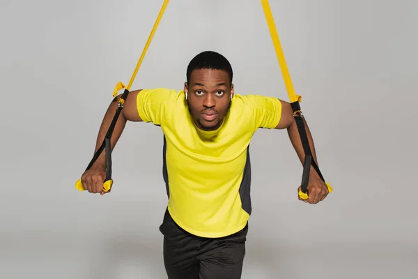 Strong african american sportsman exercising with resistance bands on grey — Stock Photo