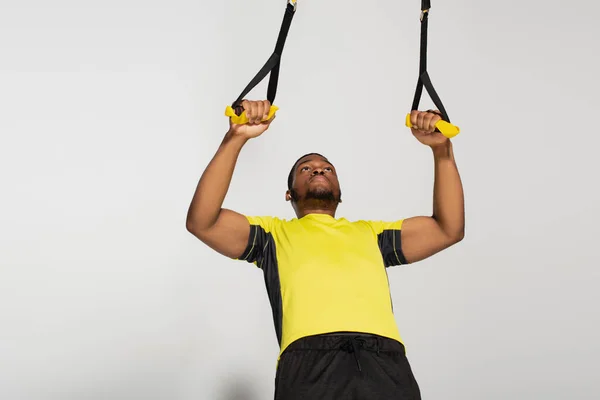 Muscular african american sportsman exercising with resistance bands on grey — Stock Photo