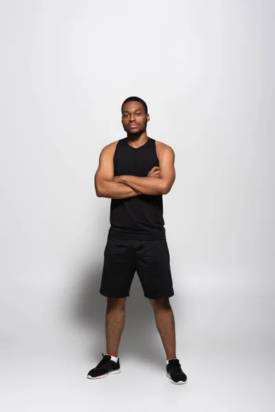 Longitud completa del deportista afroamericano en camiseta sin mangas y pantalones cortos de pie con los brazos cruzados en gris - foto de stock