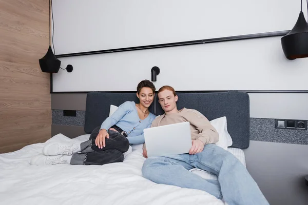 Cheerful couple using laptop on bed in hotel room — Stock Photo