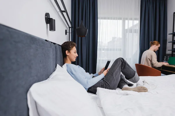 Seitenansicht der Frau mit digitalem Tablet mit leerem Bildschirm in der Nähe ihres Freundes im Hotelzimmer — Stockfoto