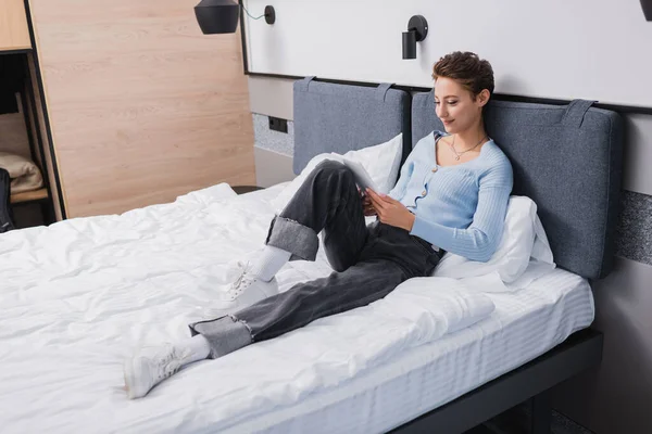 Young woman using digital tablet on bed in hotel room — Foto stock