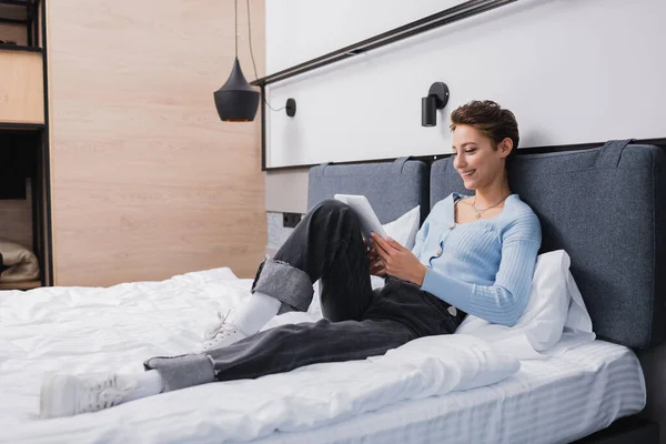 Femme positive utilisant une tablette numérique sur le lit dans la chambre d'hôtel — Photo de stock