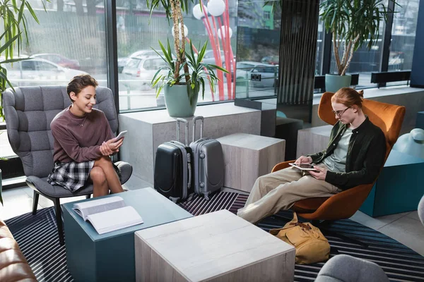 Young couple using smartphone and digital tablet near suitcases in hotel lobby — Stock Photo