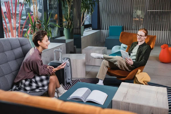 Casal sorridente usando gadgets perto de malas no lobby do hotel — Fotografia de Stock