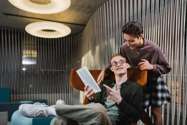 Hombre sonriente apuntando a la tableta digital cerca de la novia en el vestíbulo del hotel - foto de stock