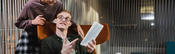 Young man pointing at digital tablet near girlfriend in hotel lobby, banner — Stock Photo