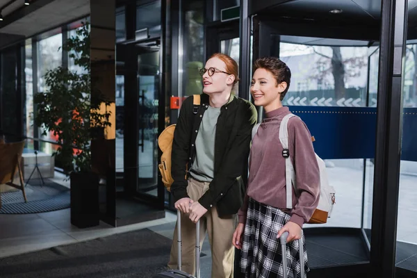 Positive couple with suitcases and backpacks standing in hotel lobby — Fotografia de Stock