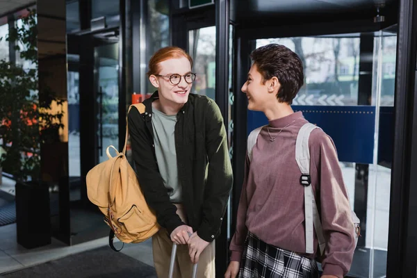 Cheerful man with suitcase and backpack looking at girlfriend in hotel — Stock Photo