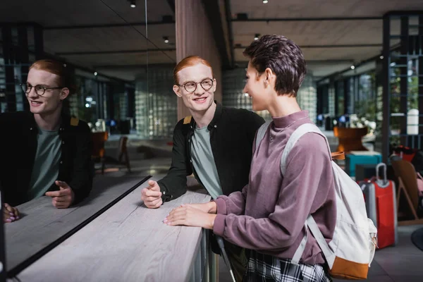 Cheerful couple with backpack and suitcase standing near hotel reception — Stock Photo